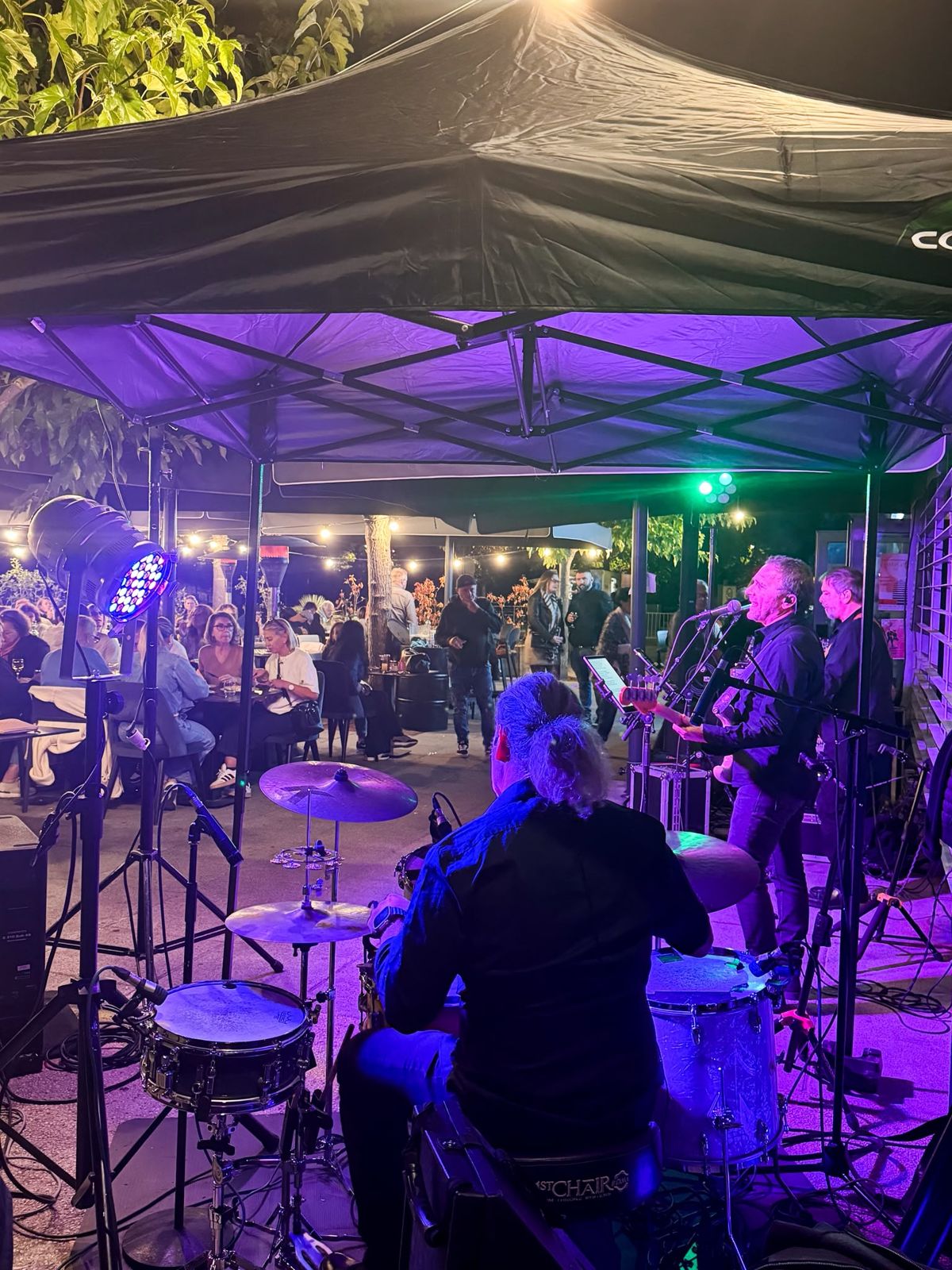 Groupe de musiciens jouant en concert sur la terrasse du Café de la Place, en soirée
